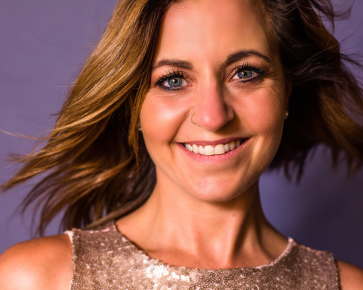 A smiling client with her hair blowing, against a purple backdrop
