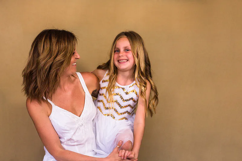 A mother holding her daughter, both smiling, against a warm gold backdrop