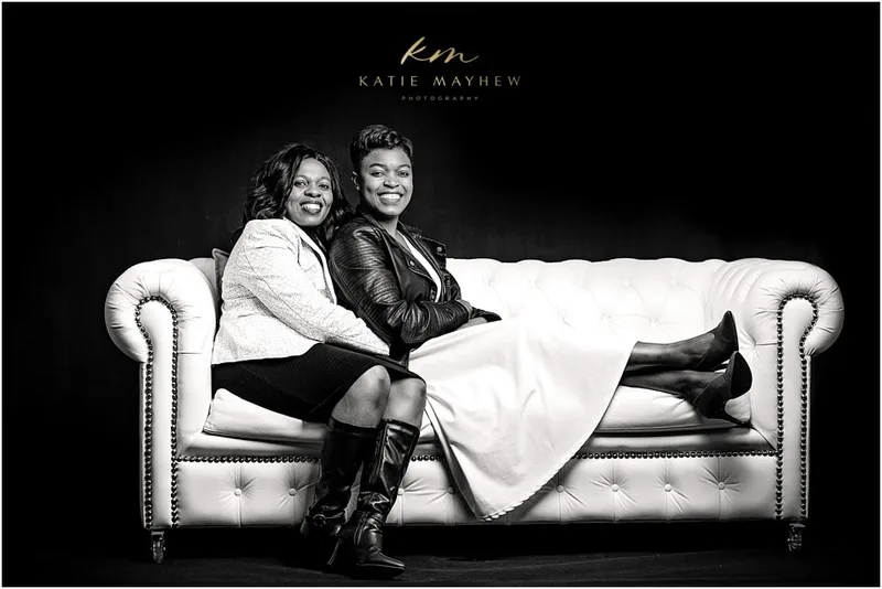 A black and white portrait of a mother and her grown daughter on a white couch